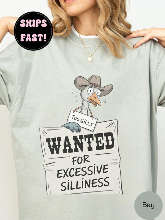 A person wearing a gray t-shirt with a cartoon image of a bird, holding a sign that says "Too Silly" and "Wanted for Excessive Silliness".