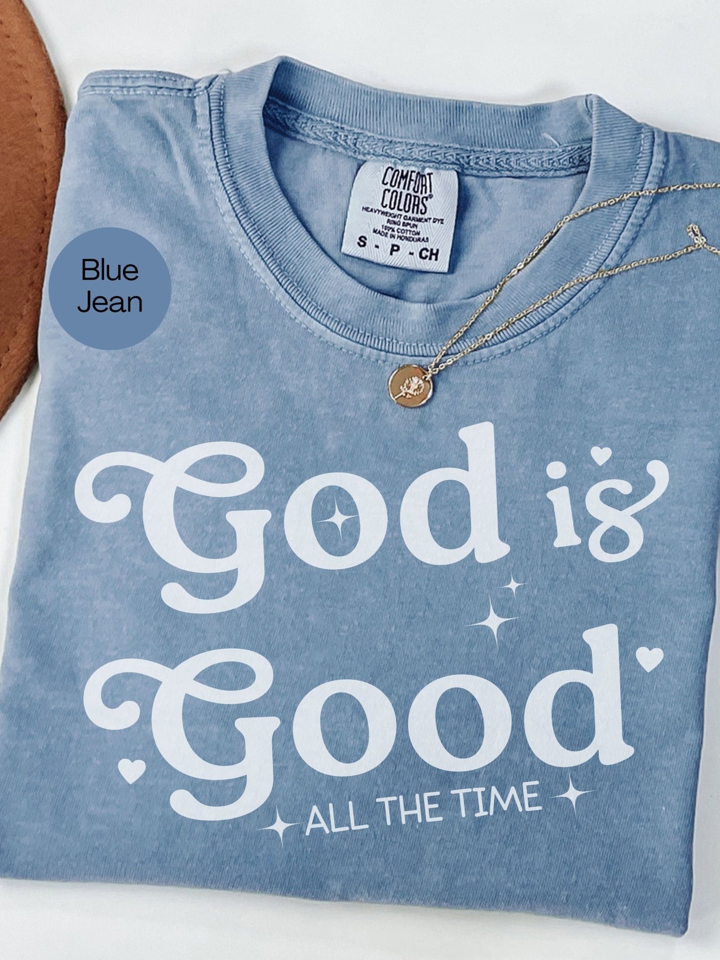 A blue t-shirt with the text "God is Good" printed on it, along with a small gold pendant necklace.