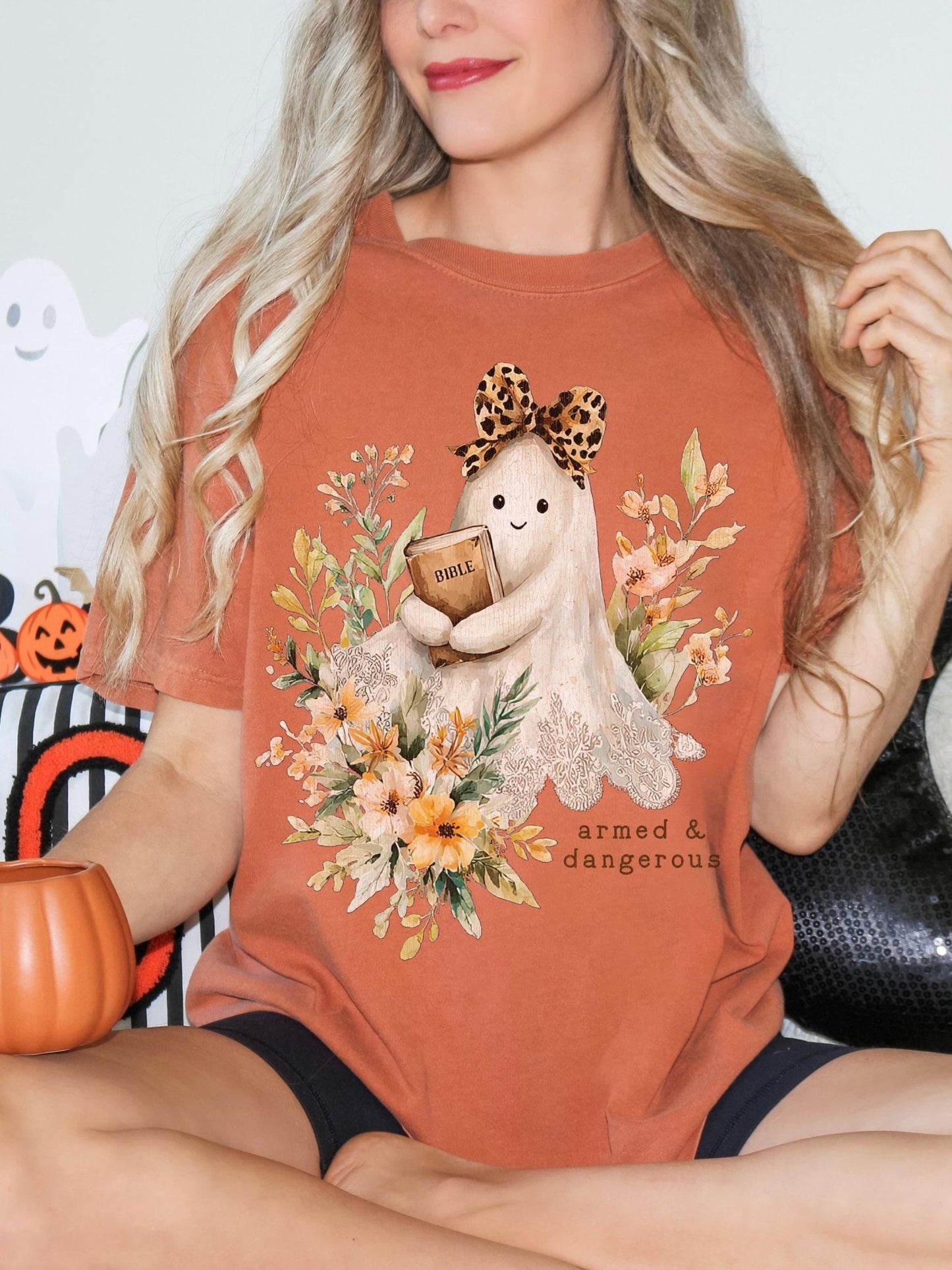 A woman wearing a t-shirt with a graphic of a ghost holding a book and surrounded by flowers.