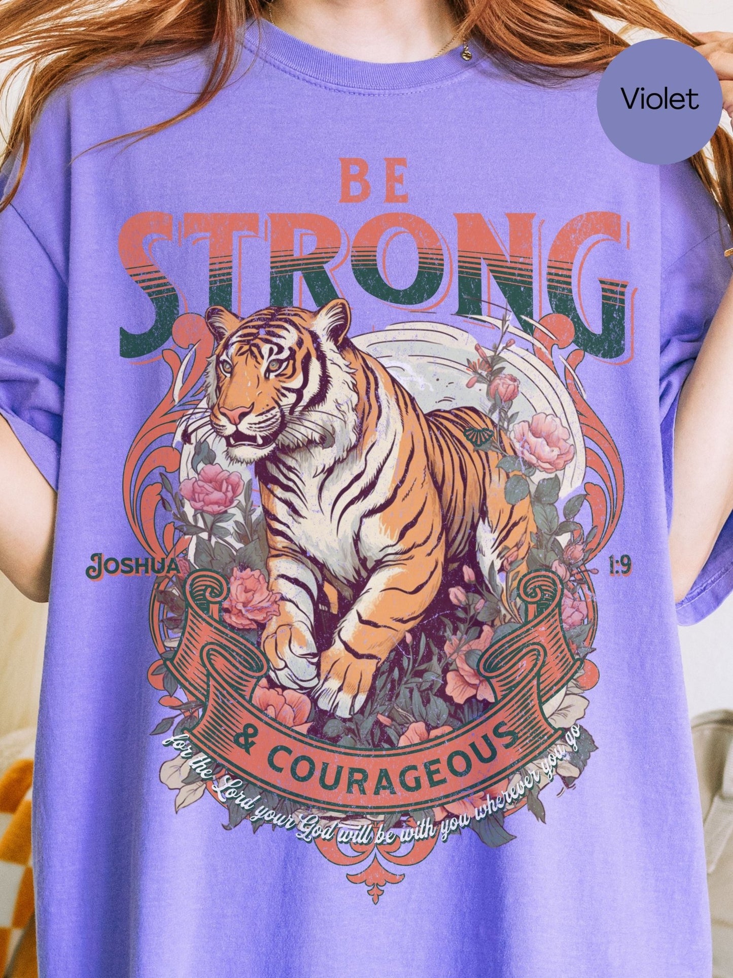 A person wearing a purple t-shirt with a graphic design featuring a tiger surrounded by flowers and text.