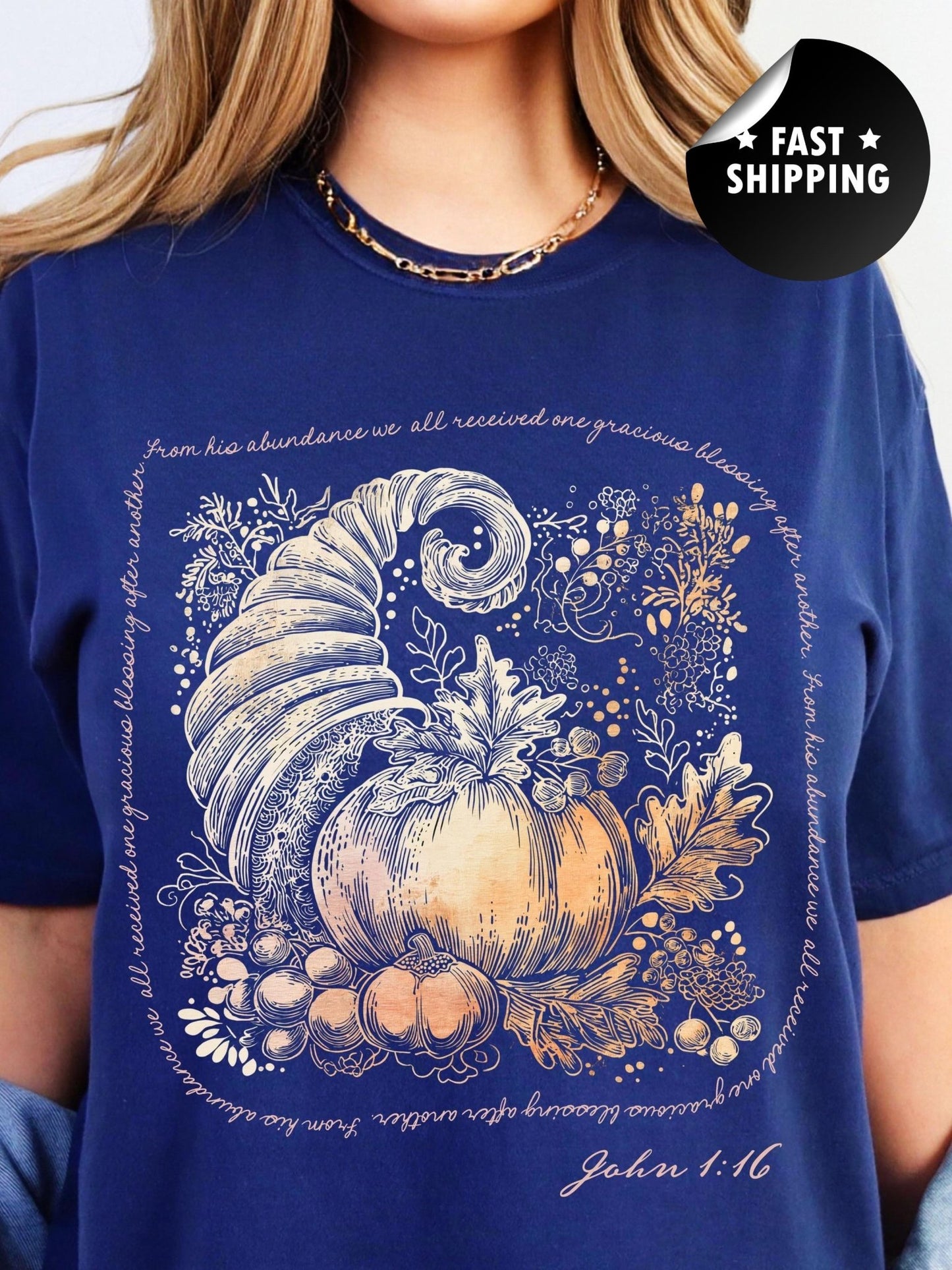 A woman wearing a blue t-shirt with a graphic design depicting a golden cornucopia surrounded by autumn leaves and pumpkins.