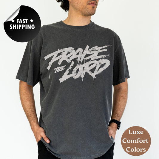 A man wearing a grey t-shirt with the text &quot;PRAISE THE LORD&quot; printed on it.