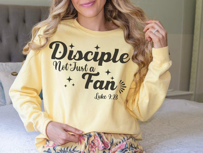 A woman wearing a yellow sweatshirt with the text &quot;Disciples Not Just Fans&quot; printed on it.