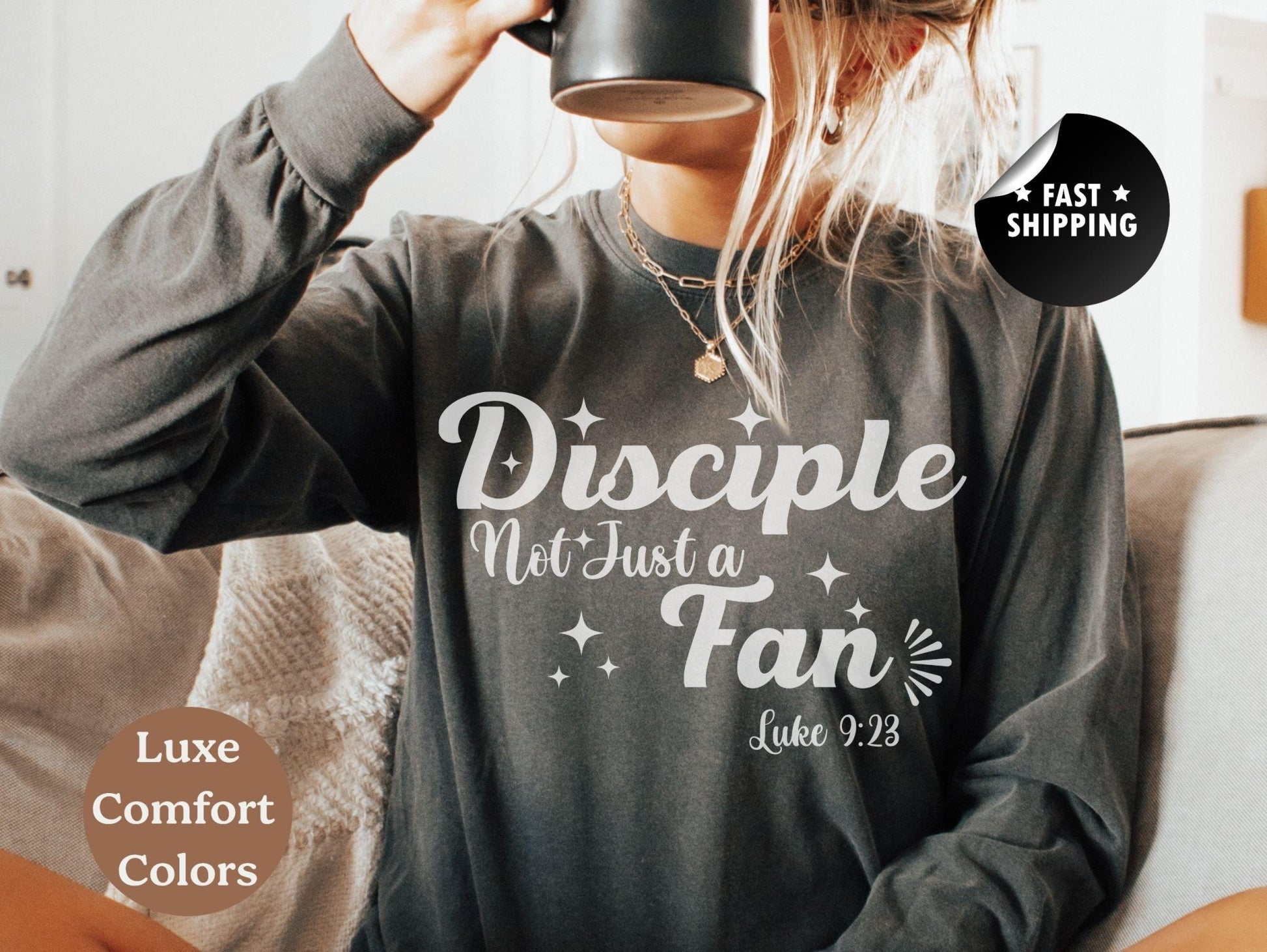 A person wearing a gray long-sleeved shirt with white text and a graphic design, sitting on a couch and holding a black mug.