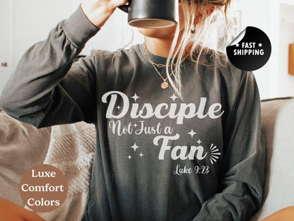 A person wearing a gray long-sleeved shirt with white text and a graphic design, sitting on a couch and holding a black mug.