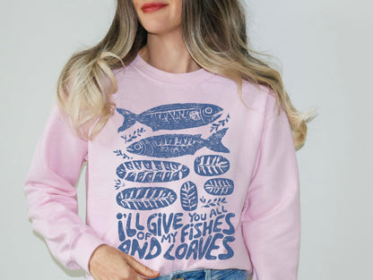 A woman wearing a pink sweatshirt with a graphic design of fish and the text &quot;I&#39;ll give you all of my fish and loaves&quot;.