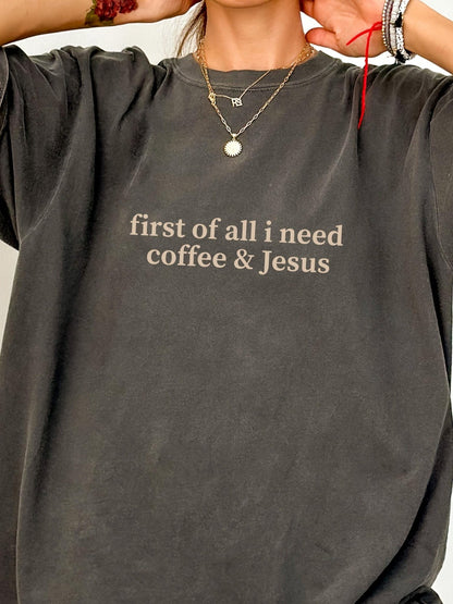 A person wearing a gray t-shirt with the text "first of all I need coffee & Jesus" printed on it.