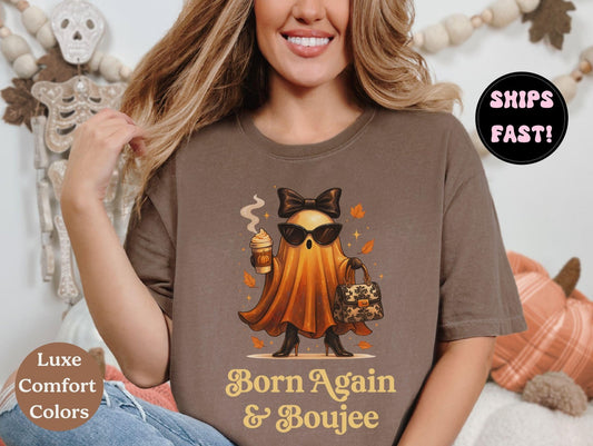 A woman wearing a brown t-shirt with a graphic of a ghost character and the text "Born Again & Boujee" is smiling.