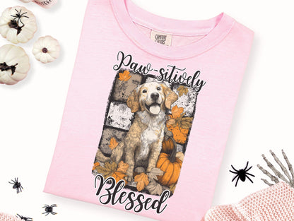 a pink t-shirt with a graphic design of a dog surrounded by autumn leaves and pumpkins, along with the text "Paw sitively Blessed" printed on it.