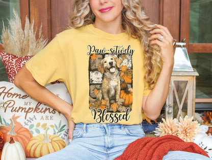 A woman wearing a yellow t-shirt with a graphic of a dog and autumn leaves, sitting on a bench surrounded by fall decorations.