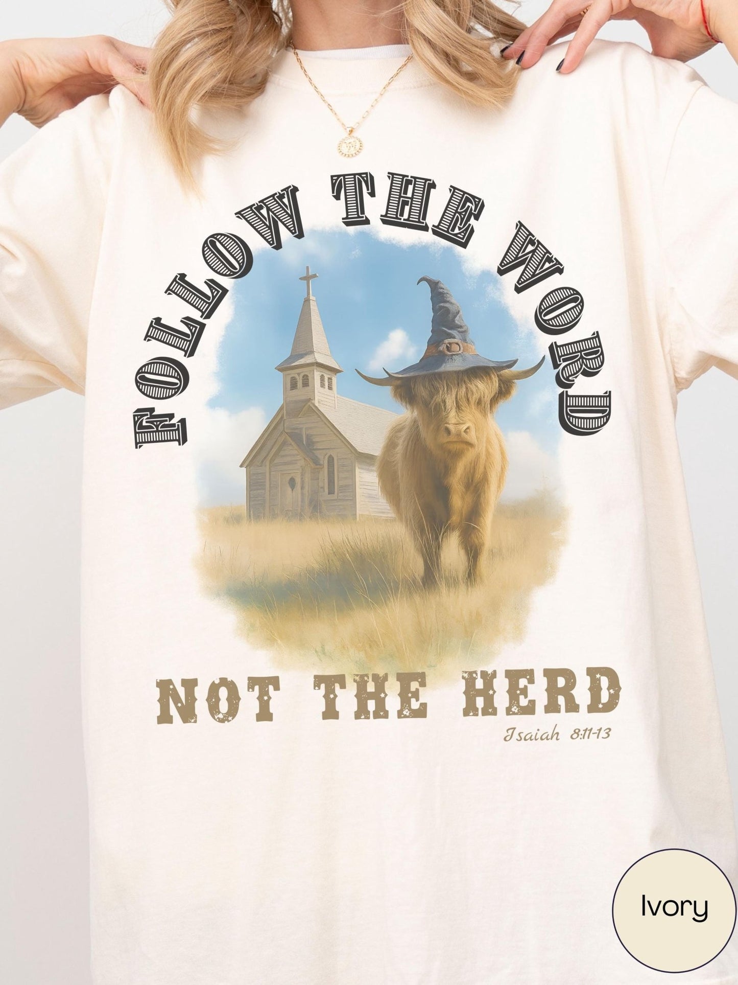 A person wearing a white t-shirt with a graphic design featuring a cow wearing a witch&#39;s hat and the text &quot;FOLLOW THE WORD NOT THE HERD&quot; along with a church in the background.
