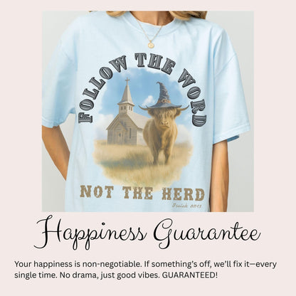 A person wearing a light blue t-shirt with a graphic design featuring a cow wearing a witch's hat and the text "FOLLOW THE WORD NOT THE HERD" along with a Bible verse reference.