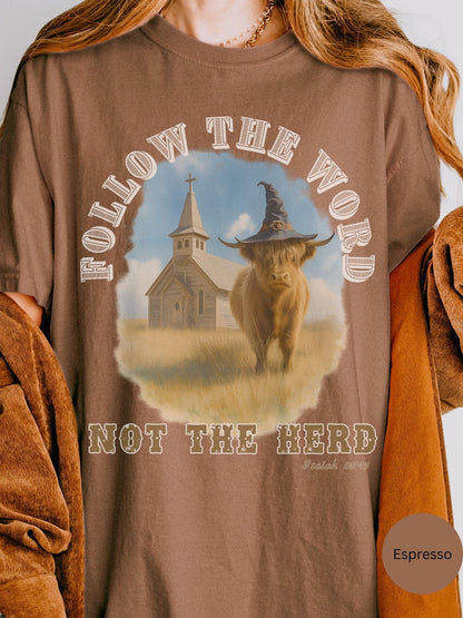 a t-shirt with a graphic design depicting a cow wearing a witch&#39;s hat, standing in front of a church. The text on the t-shirt reads &quot;FOLLOW THE WORD NOT THE HERD&quot; and &quot; Isaiah 55:11&quot;.