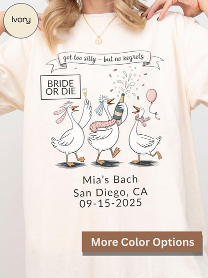 A white t-shirt with a graphic design featuring three cartoon geese, one of which is holding a champagne bottle, celebrating what appears to be a wedding or engagement party.