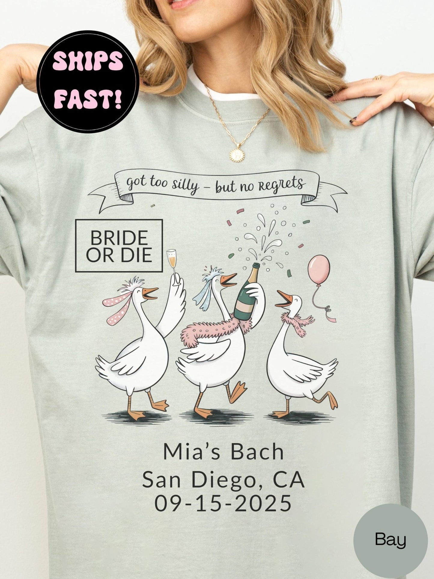 A woman wearing a gray t-shirt with a graphic design featuring three cartoon geese and text related to a wedding event.