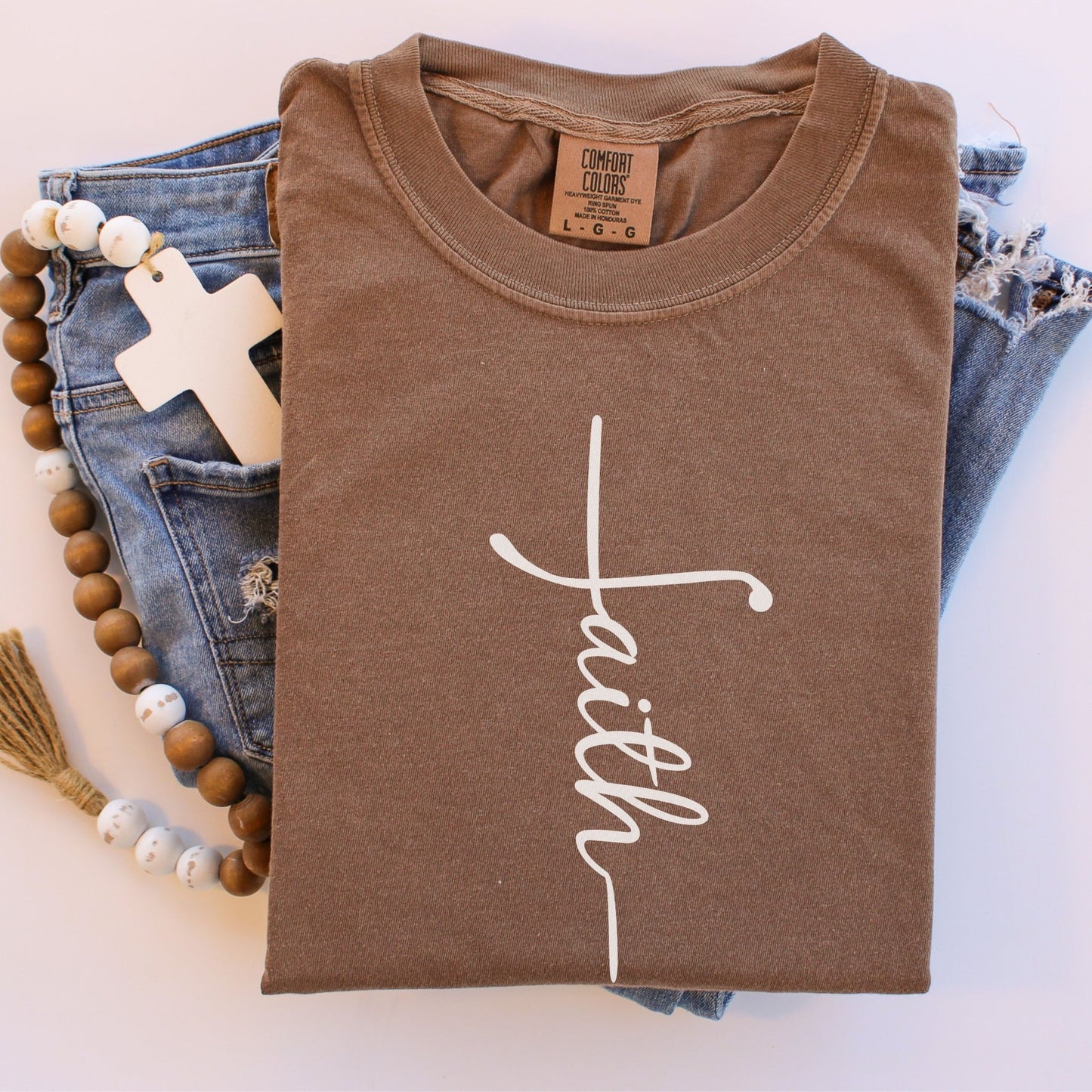 a brown t-shirt with the word "Faith" written in white cursive text, along with a pair of blue jeans and a beaded necklace.