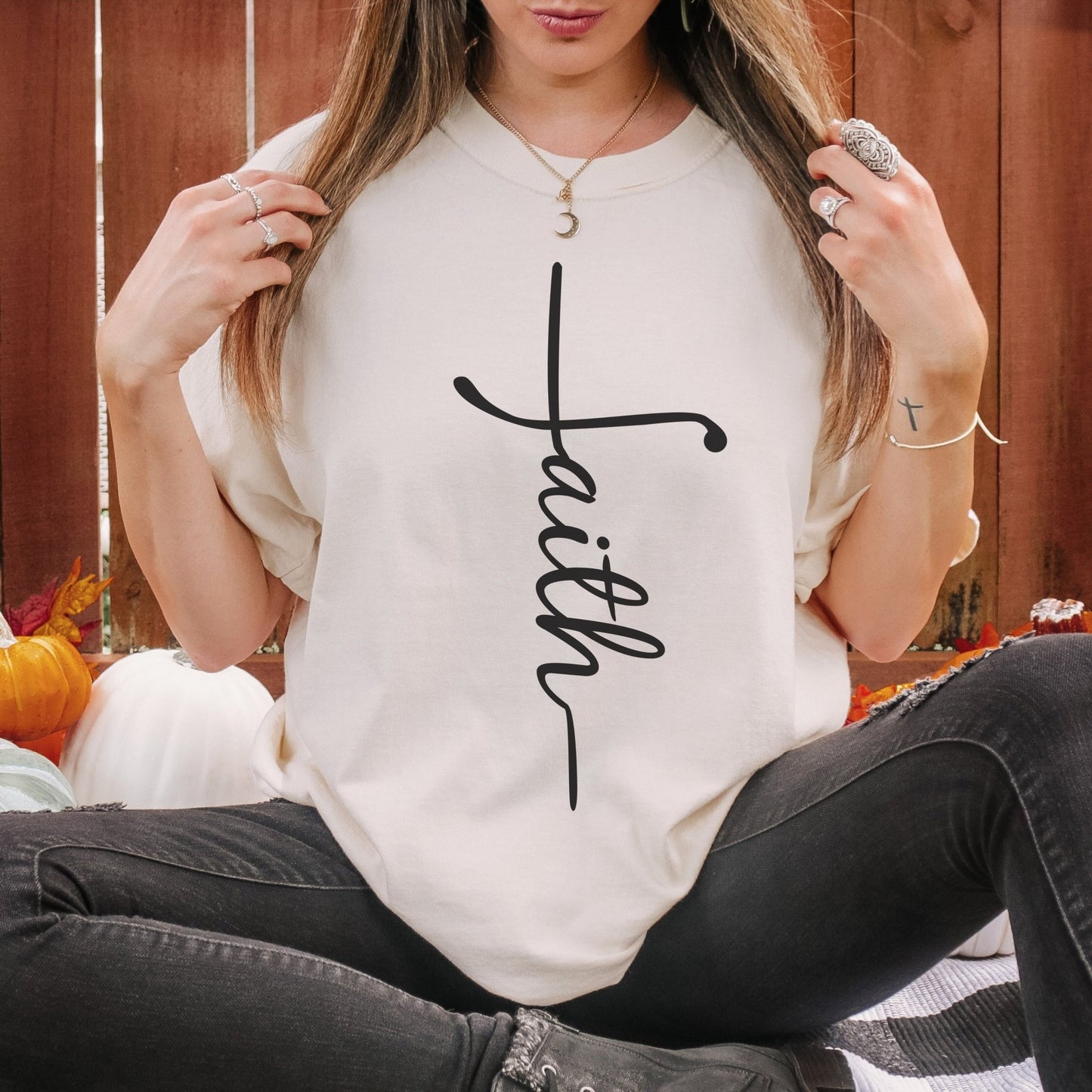 A woman wearing a white t-shirt with the word "Faith" printed on it, sitting on a bench with her hands behind her back.