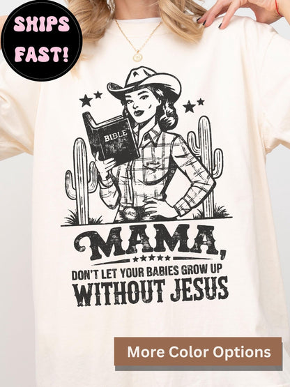 A white t-shirt with a graphic design featuring a woman in a cowboy hat holding a Bible, along with the text "MAMA, DON'T LET YOUR BABIES GROW UP WITHOUT JESUS".