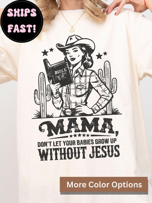 A white t-shirt with a graphic design featuring a woman in a cowboy hat holding a Bible, along with the text "MAMA, DON'T LET YOUR BABIES GROW UP WITHOUT JESUS".