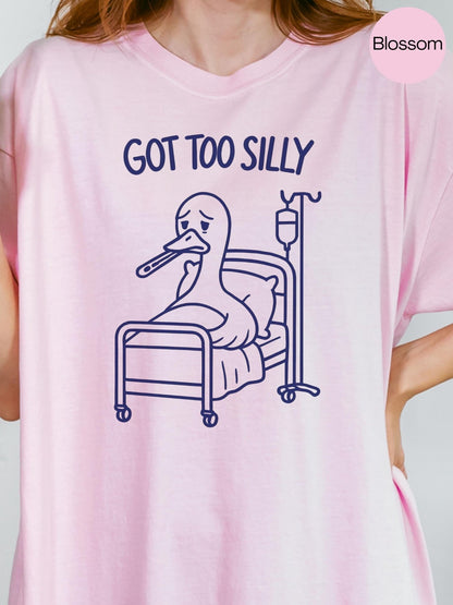 A pink t-shirt with a cartoon image of a duck in a hospital bed, accompanied by the text &quot;GOT TOO SILLY&quot;.