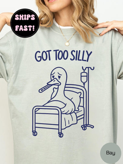 A woman wearing a gray t-shirt with a graphic of a cartoon duck in a hospital bed, with the text &quot;SHIPS FAST!&quot; and &quot;GOT TOO SILLY&quot; printed on it.