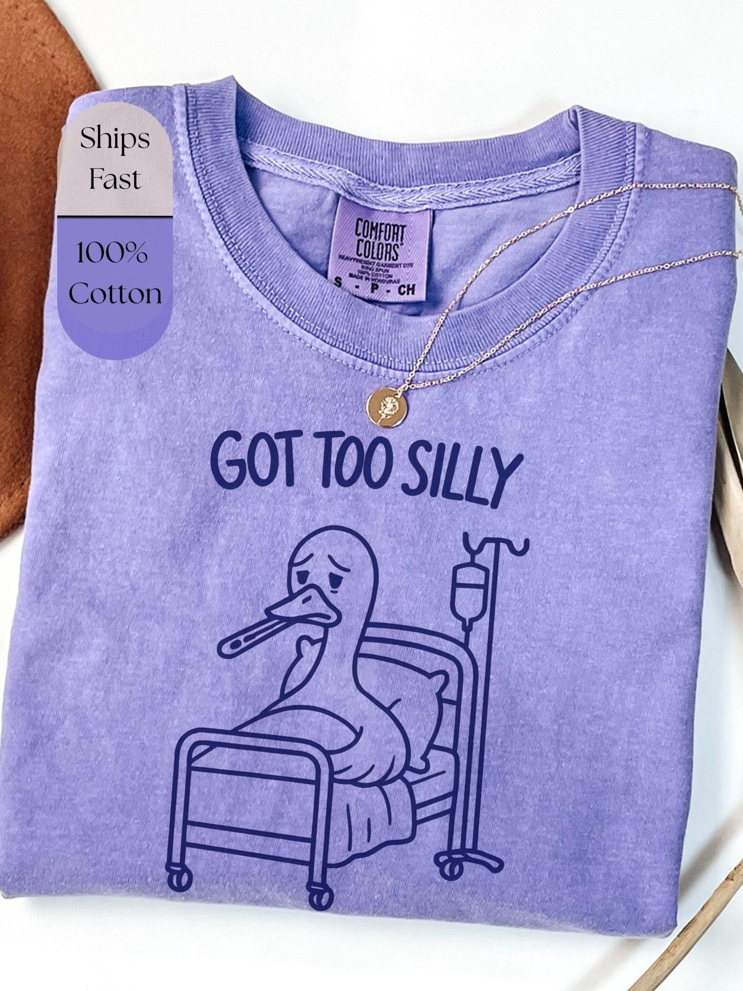 a purple t-shirt with a cartoon duck in a hospital bed, accompanied by the text &quot;GOT TOO SILLY&quot; printed on it.