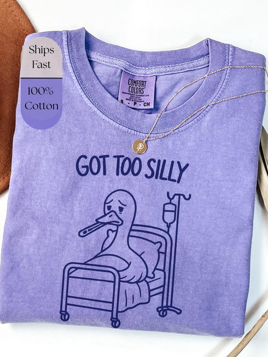 a purple t-shirt with a cartoon duck in a hospital bed, accompanied by the text &quot;GOT TOO SILLY&quot; printed on it.