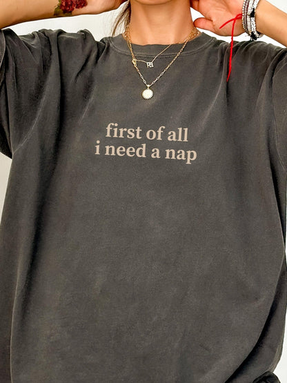 A person wearing a gray t-shirt with the text "first of all I need a nap" printed on it.
