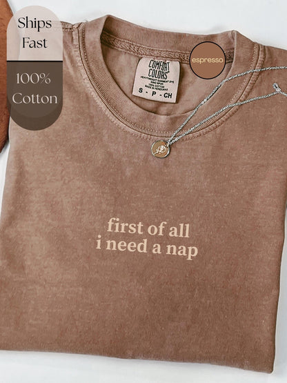 A brown t-shirt with the text "first of all I need a nap" printed on it, along with a small charm necklace.