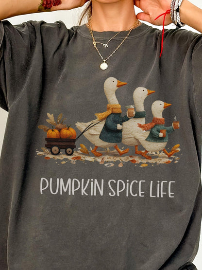 A person wearing a gray t-shirt with a graphic design depicting three white ducks walking on a path, each carrying a pumpkin and holding a cup of spice. The text below the image says &quot;PUMPKIN SPICE LIFE&quot;.