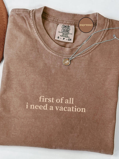 A brown t-shirt with the text "first of all I need a vacation" printed on it, along with a small charm necklace.