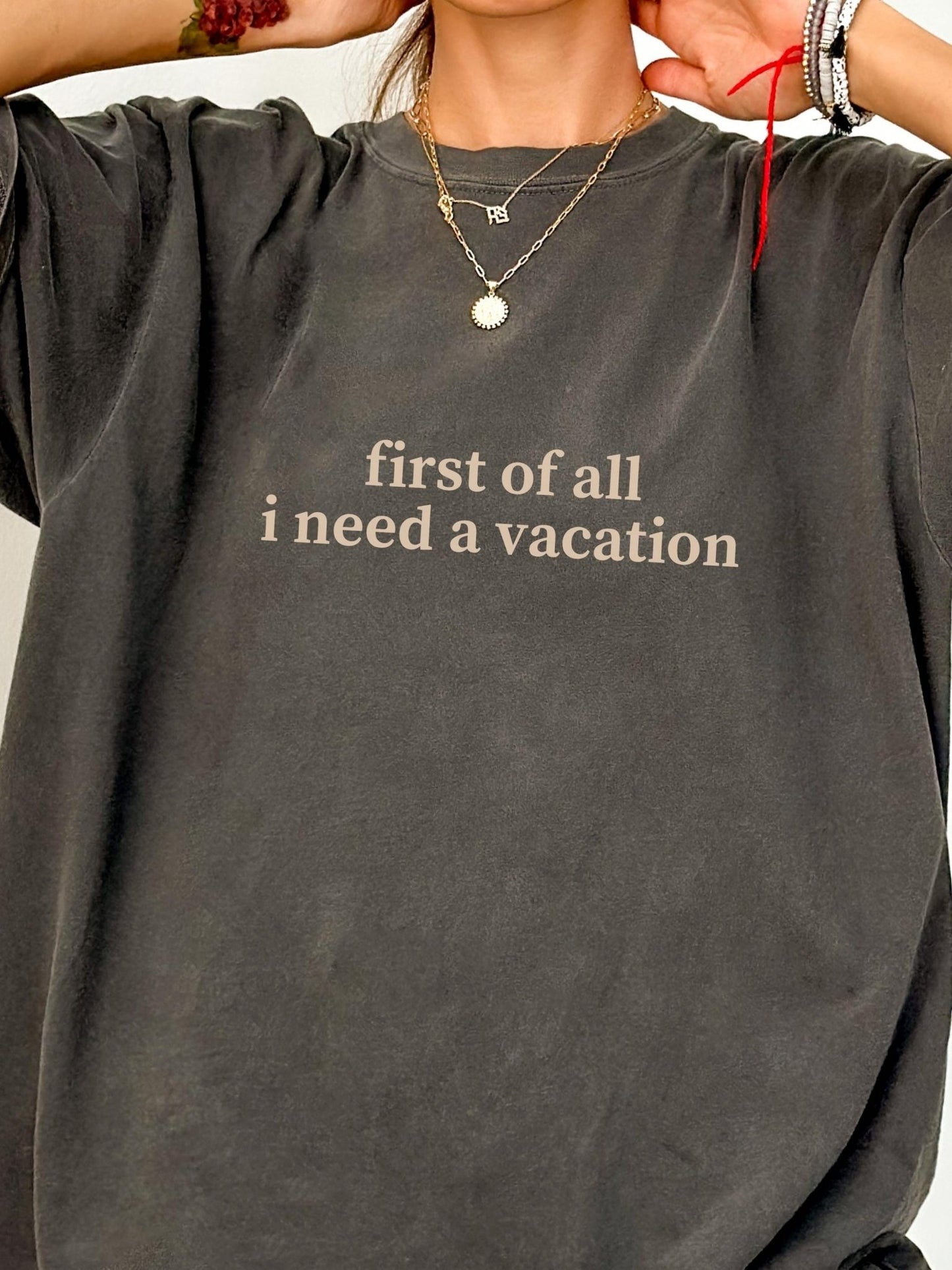 A person wearing a gray t-shirt with the text "first of all I need a vacation" printed on it.