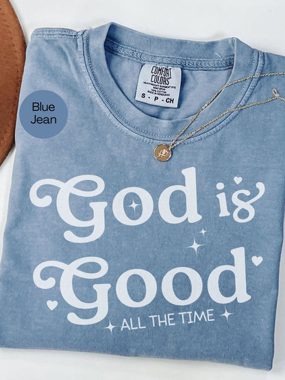 A blue t-shirt with the text "God is Good" printed on it, along with a small gold pendant necklace.