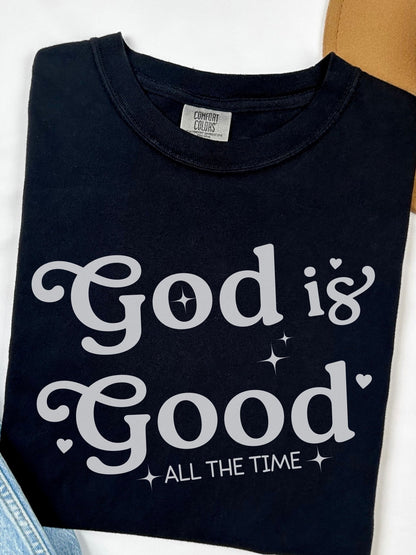 A black t-shirt with white text that says "God is Good" and "All the Time".