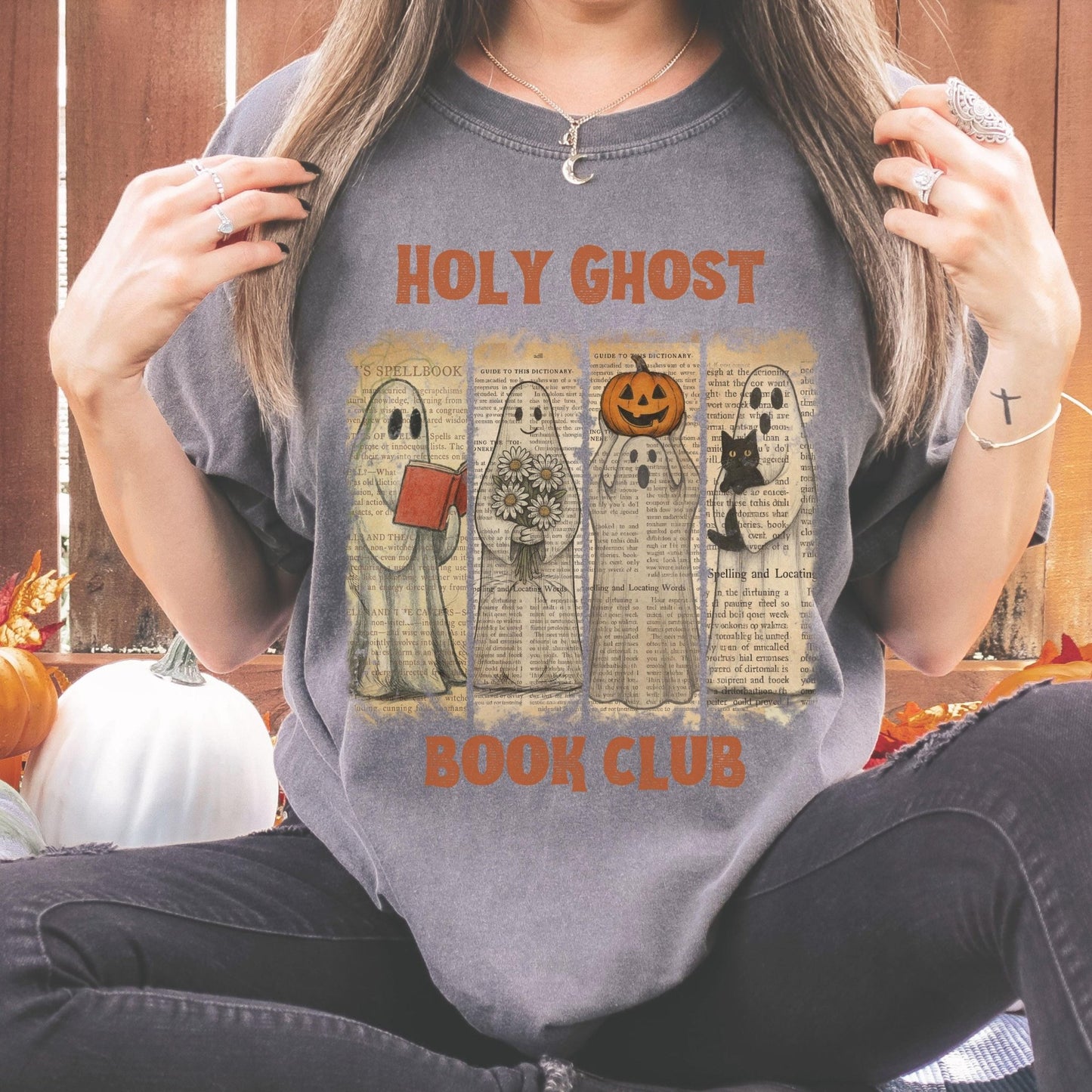 A person wearing a gray t-shirt with a graphic design featuring five ghost characters and the text "HOLY GHOST BOOK CLUB".