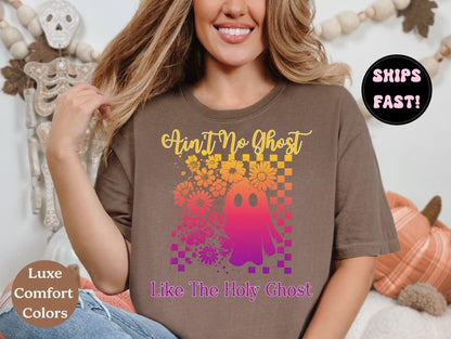 A woman wearing a brown t-shirt with a graphic design featuring a ghost and flowers, smiling and posing in front of a Halloween decoration.