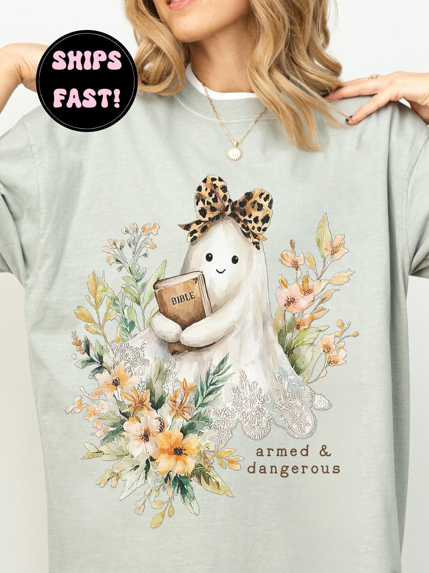 A woman wearing a light green t-shirt with a graphic design of a ghost holding a book and surrounded by flowers.