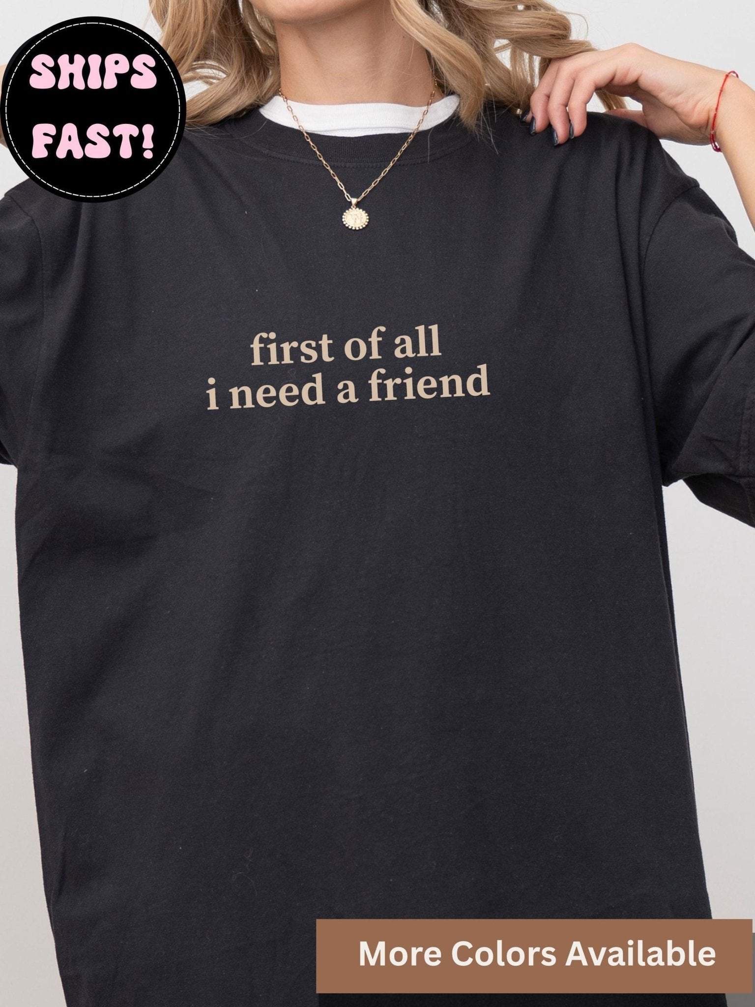 a person wearing a black t-shirt with the text &quot;first of all I need a friend&quot; printed on it.