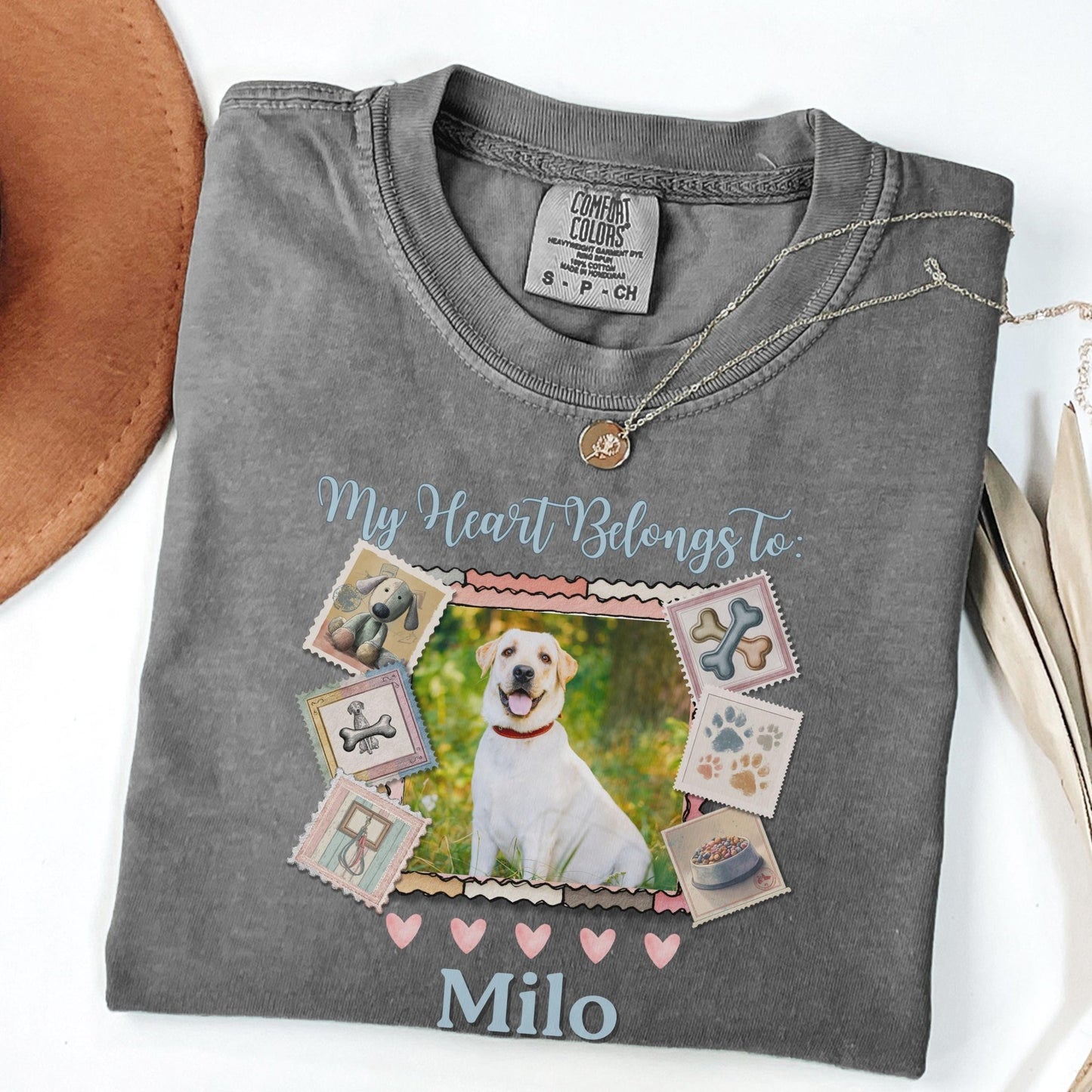 A gray t-shirt with a collage of dog-related images and text, including a dog, bones, and a bowl, along with the text &quot;My Heart Belongs To Milo&quot;.