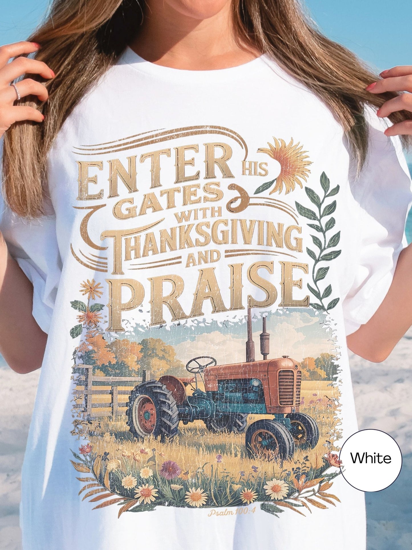 A white t-shirt with a graphic design featuring a tractor in a field, surrounded by flowers and leaves, along with a Bible verse from Psalm 100:4.
