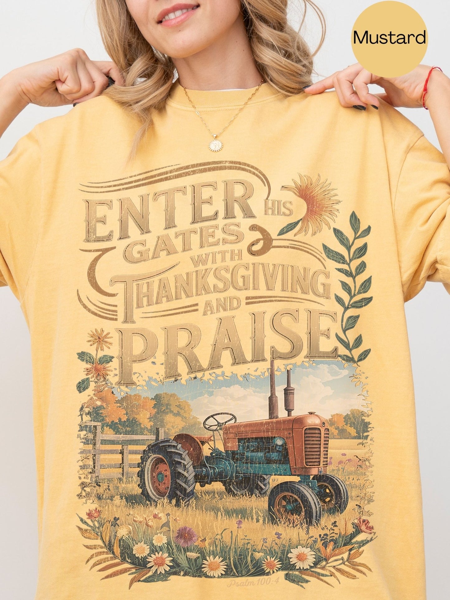 A woman wearing a yellow t-shirt with a graphic design depicting a tractor in a field with flowers and a message about entering gates with Thanksgiving and praise.