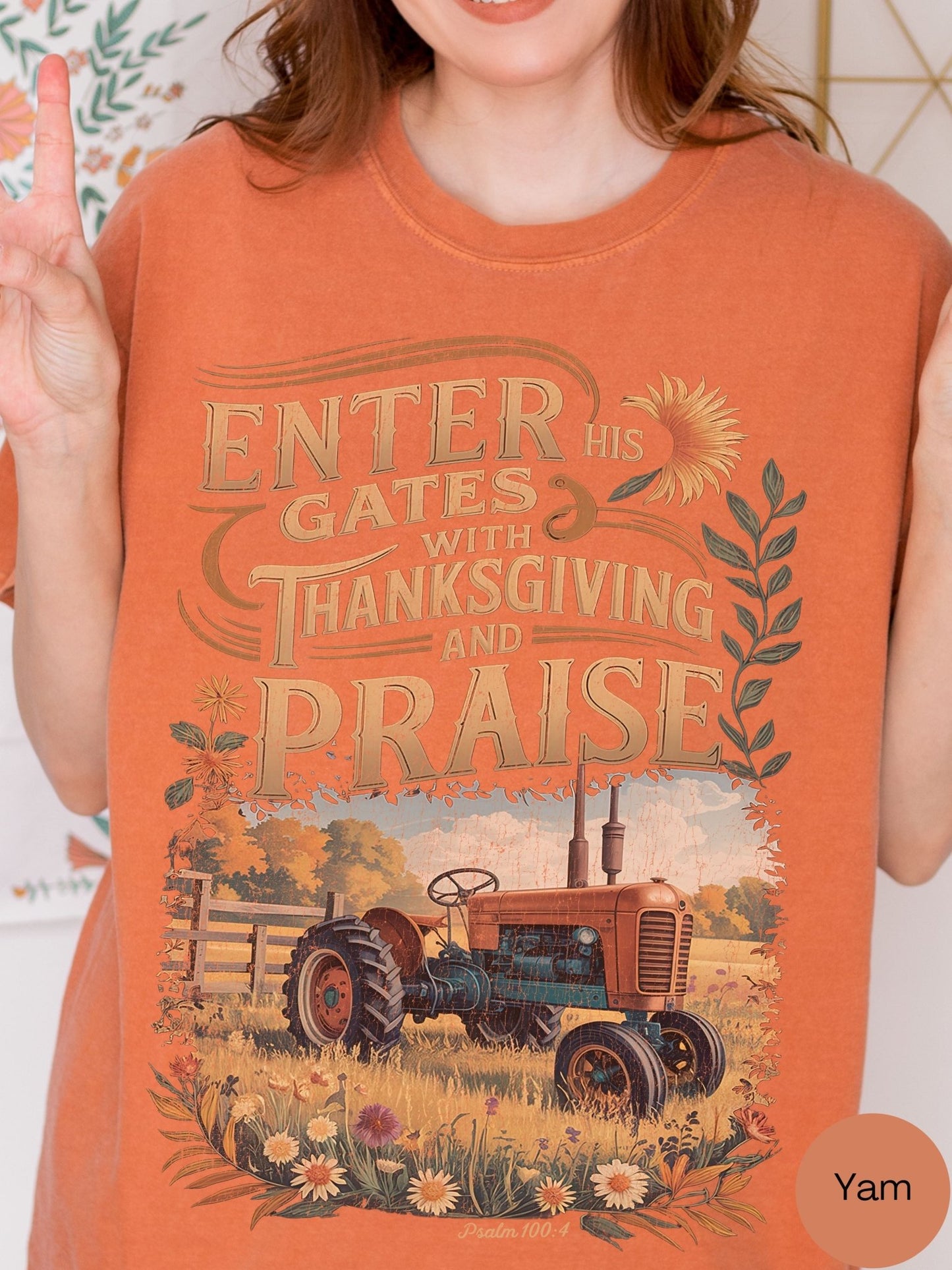 a woman wearing an orange t-shirt with a graphic design depicting a tractor in a field, along with text that reads "Enter his gates with Thanksgiving and praise".