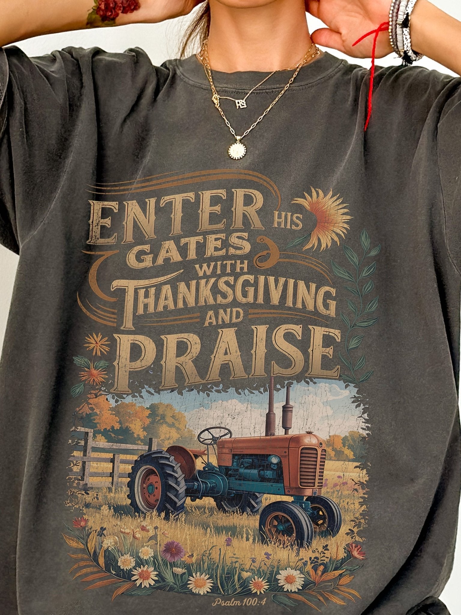 a person wearing a grey t-shirt with a graphic design depicting a tractor in a field, along with text that reads "ENTER his GATES with THANKSGIVING and Praise".