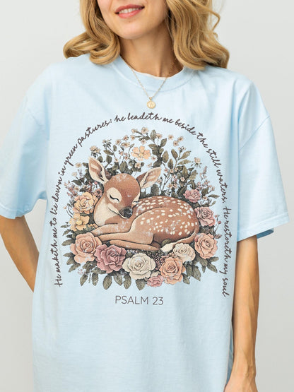 A woman wearing a light blue t-shirt with a printed design of a sleeping deer surrounded by flowers and text.