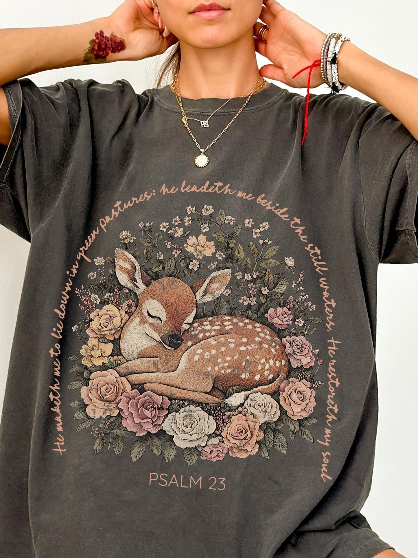 A person wearing a gray t-shirt with a graphic design of a sleeping deer surrounded by flowers and text.