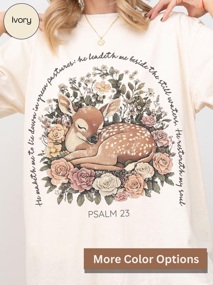 A person wearing a white t-shirt with a printed design of a sleeping deer surrounded by flowers and greenery.
