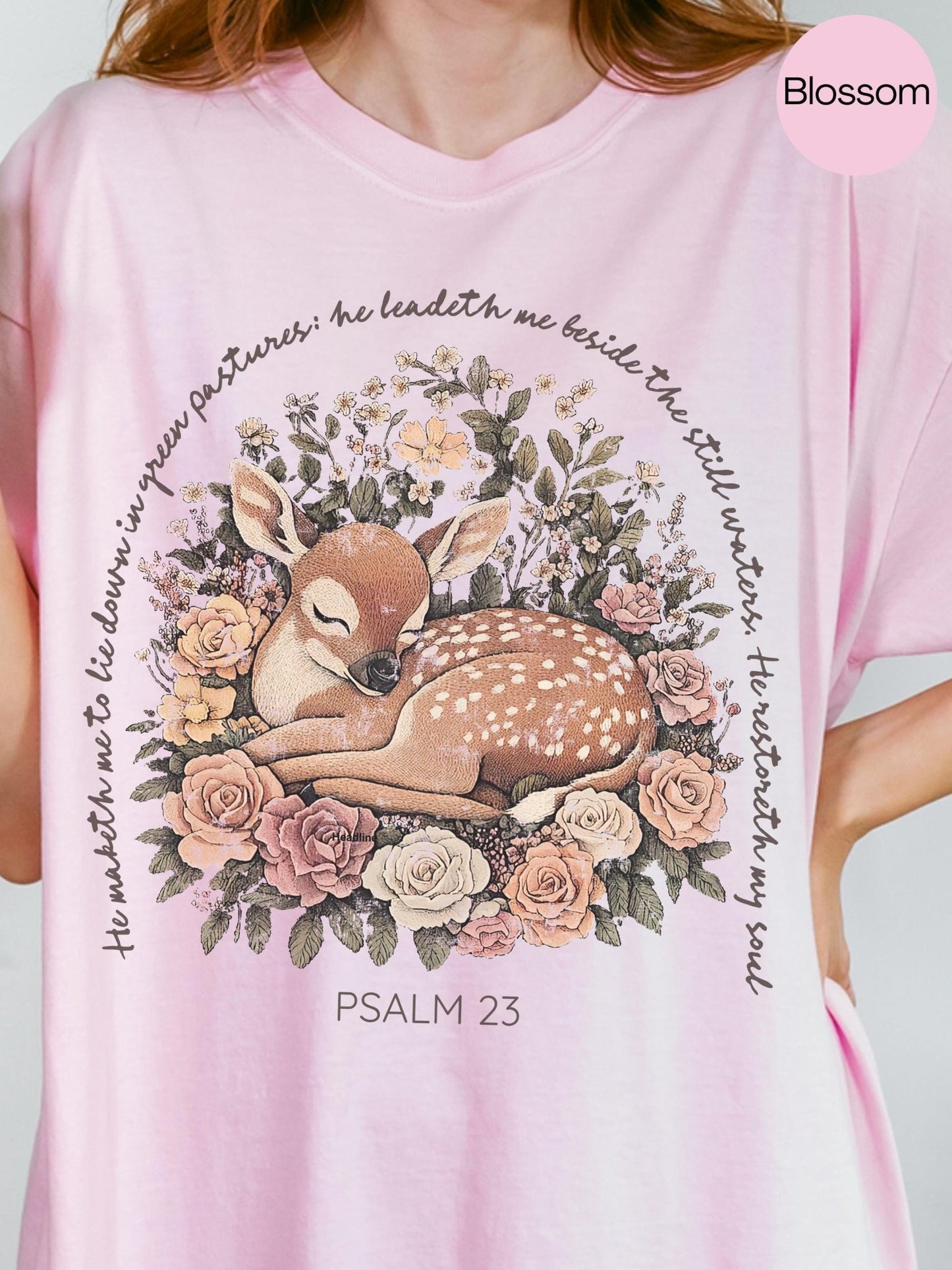A woman wearing a pink t-shirt with a graphic design of a sleeping deer surrounded by flowers and greenery.