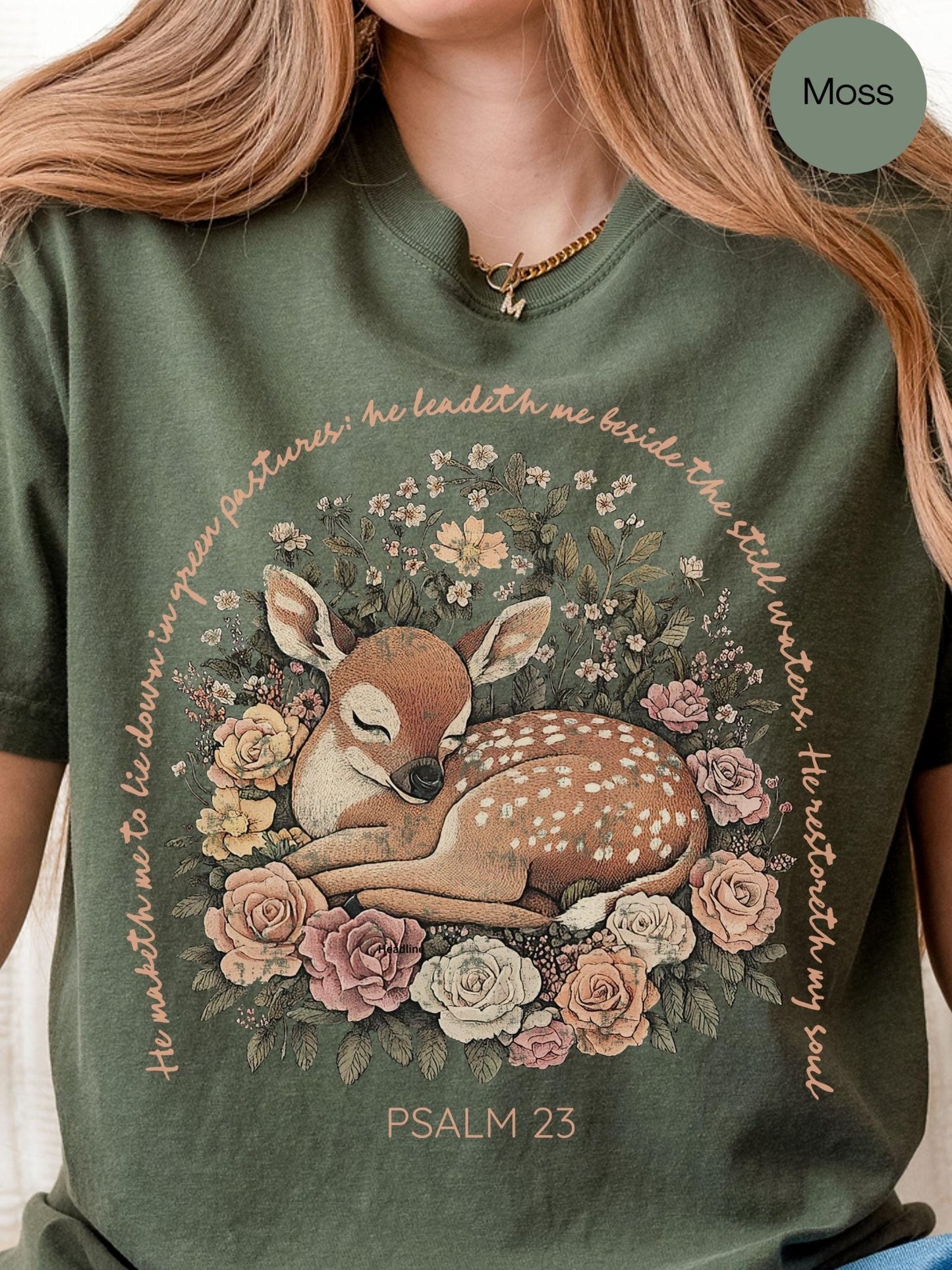 A woman wearing a green t-shirt with a printed design of a sleeping deer surrounded by flowers and greenery.