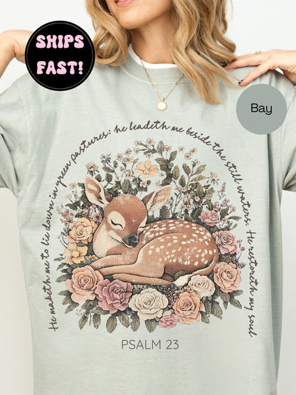 a woman wearing a gray t-shirt with a floral design and a Bible verse from Psalm 23 printed on it.