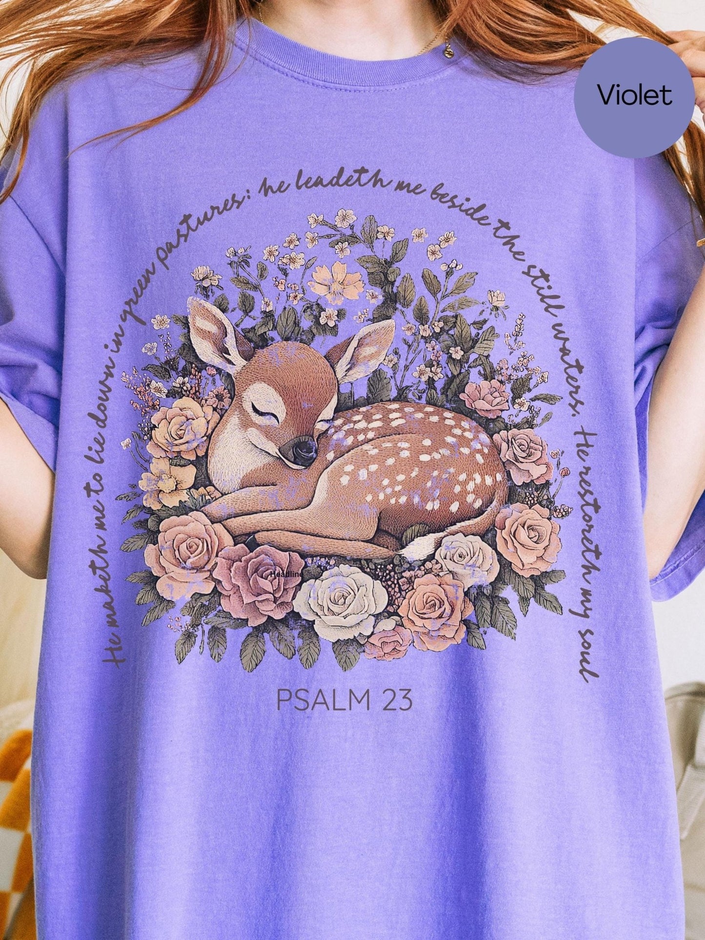 A person wearing a purple t-shirt with a graphic design depicting a sleeping deer surrounded by flowers and greenery.